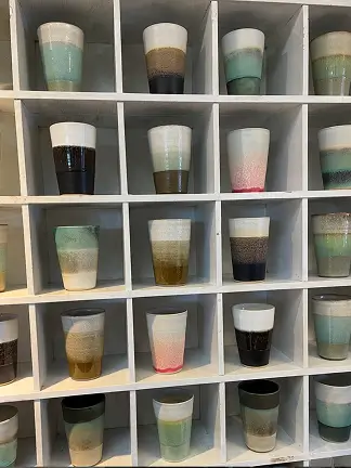 Krus i forskellige farver og glasurer i rumopdelt reol – brugt på forsiden.